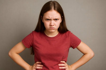 Studio portrait featuring a teenage girl showing frustration and anger, with hands on hips and a scowling expression against a gray backgroundの素材