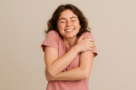 Studio portrait of a cheerful young woman embracing herself with closed eyes, showing self love and confidenceの素材