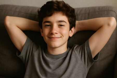 Relaxed teen lying on a sofa with hands behind his head, smiling happily and enjoying a carefree moment of comfort and rest indoorsの素材