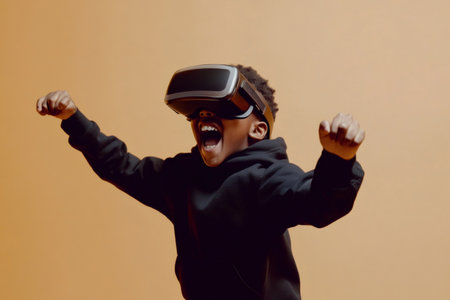 Young boy wearing vr headset is playing a videogame and expressing excitement with raised fists and open mouthの素材