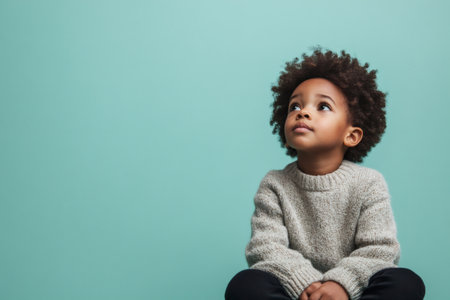 Young boy looking up with a thoughtful expression, evoking curiosity and childhood wonder against a vibrant backdropの素材