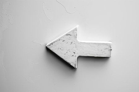 High-contrast photo of a minimalist white arrow pointing left on a textured gray surfaceの素材