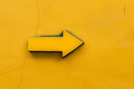 Bold yellow arrow pointing right against a textured yellow wallの素材