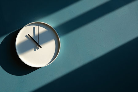 Photo of a sleek, minimalist clock casting a bold shadow on a blue wallの素材