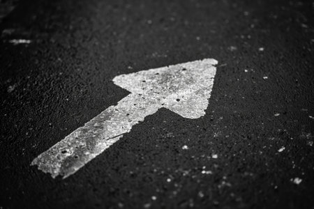 Minimalist black and white photo of a worn arrow painted on asphalt, symbolizing directionの素材