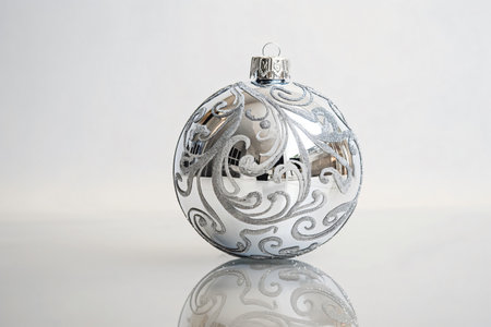 Silver Christmas ornament with an elegant floral pattern reflecting on a white backgroundの素材