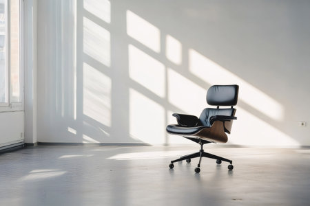 Modern, ergonomic office chair in an empty room, bathed in natural light streaming through a window, casting geometric shadows on the wall and floorの素材