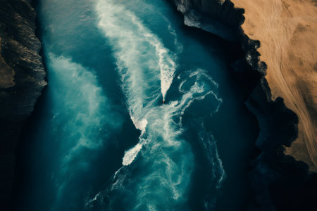 Aerial view of two rivers merging, forming beautiful patterns of turquoise and white water between dark rocky banks and a sandy shoreの素材