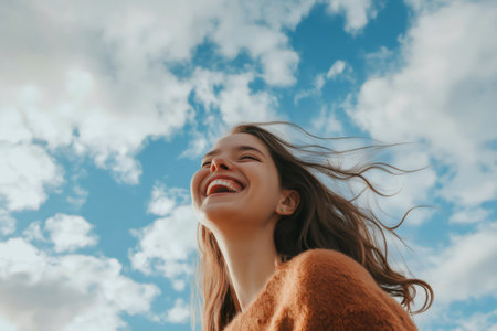 Portrait of a cheerful young woman laughing with hair blowing in the wind and cloudy sky in backgroundの素材