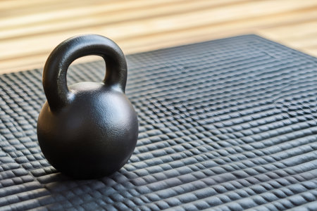Close up of a black kettlebell resting on a textured rubber mat, suggesting a fitness or weightlifting settingの素材