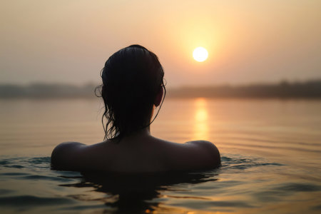 Woman immersing herself in the Ganges River during a beautiful sunset, enjoying a moment of peace and tranquilityの素材