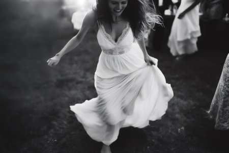 Bride in a flowing white dress dancing barefoot on lush grass, celebrating love and joy at her enchanting wedding reception under evening lightの素材