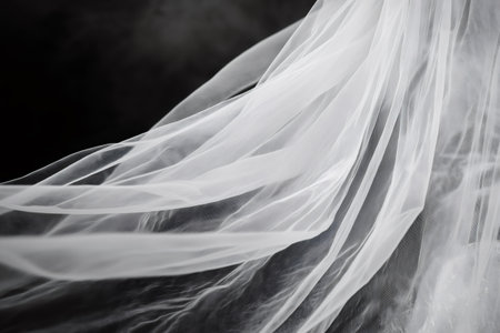 Elegant white bridal veil flowing in the wind, creating a sense of movement and grace against a dark backdropの素材