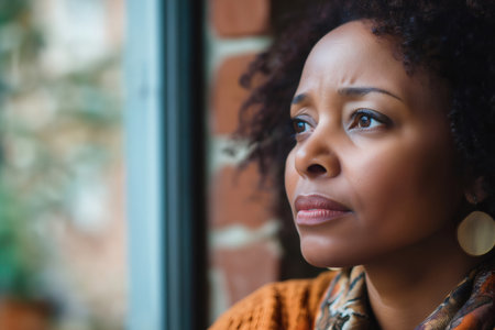 Close up of a concerned African American woman staring outside the window during a cold winter dayの素材