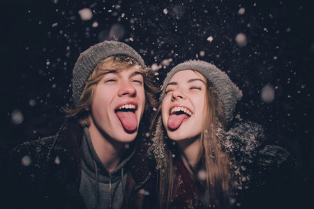 Playful young couple catching snowflakes on their tongues, laughing and enjoying a magical winter night under the starry skyの素材