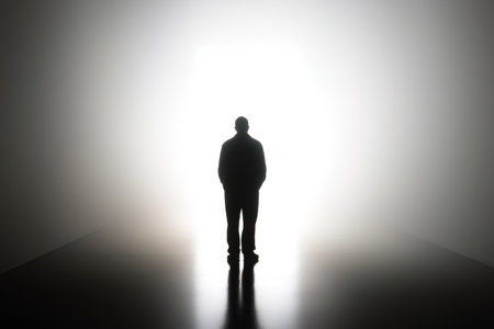 Silhouetted businessman gazing at a blinding white light emanating from the end of a dark corridor, symbolizing hope and opportunityの素材