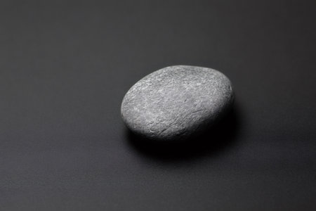 Gray pebble resting on a black background, creating a strikingly minimalist and elegant composition that highlights simplicity and textureの素材