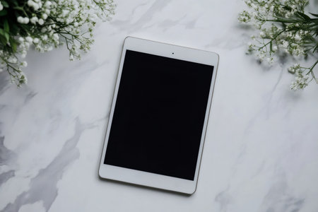 White tablet placed on a white marble table with gypsophila decorations, perfect for showcasing apps or websitesの素材