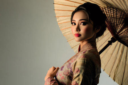 Studio portrait of a Burmese woman holding a traditional parasol, wearing traditional clothing and makeupの素材