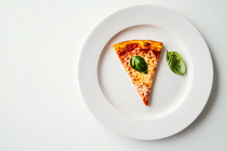 Overhead view of a single slice of margarita pizza garnished with basil leaves, served on a white plate against a minimalist white backgroundの素材