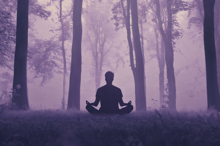Silhouetted man meditating in a foggy forest, embracing peace and mindfulness while practicing yoga among the tranquil treesの素材