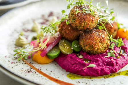 Crispy falafel balls are served on a bed of beetroot hummus, accompanied by a colorful salad, offering a visually appealing and healthy mealの素材