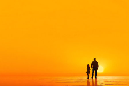 Silhouette of a father and daughter holding hands watching a beautiful orange sunset over waterの素材