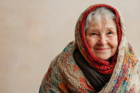Smiling senior woman wrapped in a colorful knitted headscarf and shawl, portraying warmth, tradition, and wisdomの素材