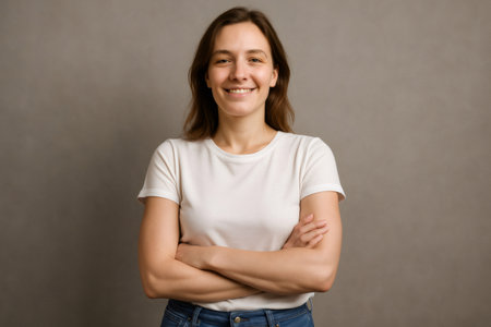 Portrait of a cheerful young woman standing with arms crossed, exuding confidence and happiness against a gray backdropの素材