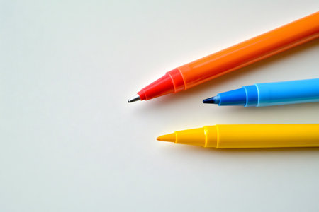 Writing and drawing tools. Three markers, yellow, blue, and orange, arranged on a bright white backgroundの素材