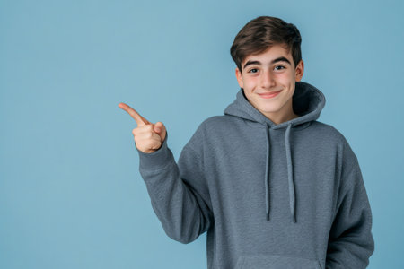 Young man wearing a gray hoodie smiling and pointing with his index finger to the left side, presenting informationの素材