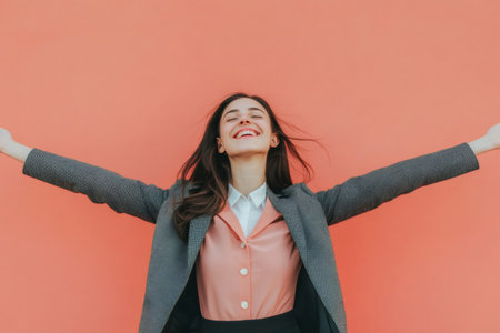 Young professional woman expressing joy and freedom with arms outstretched and a big smile against a vibrant backgroundの素材