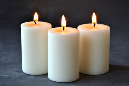 Three white pillar candles casting a warm glow in a clean, dark setting, representing peace and spiritual lightの素材