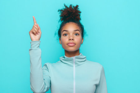 Young athletic woman with an afro bun hairstyle pointing up, indicating an idea, choice, or upwards movementの素材