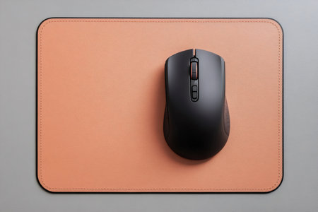 Wireless computer mouse and a textured peach colored faux leather mousepad on a gray desktop background. Top view, copy spaceの素材