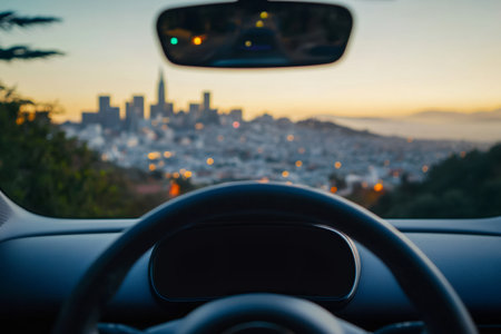 Modern car dashboard and steering wheel driving at sunset, blurry cityscape with hills and lights in backgroundの素材