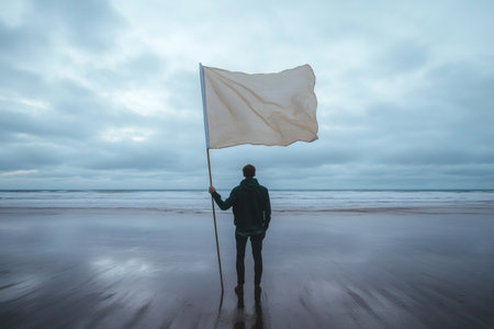 Person stands on a wet beach, holding a blank flag against a cloudy sky and ocean waves. Representing surrender or neutralityの素材