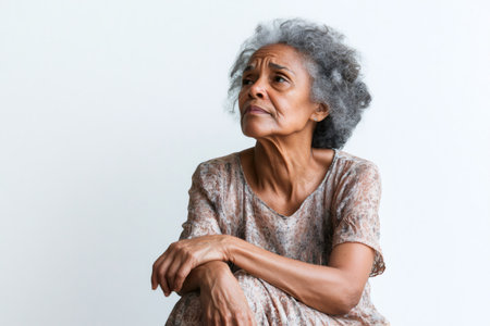 Senior mixed race woman with gray hair sitting, looking away thoughtfully. Concept of aging, contemplation, and wisdomの素材