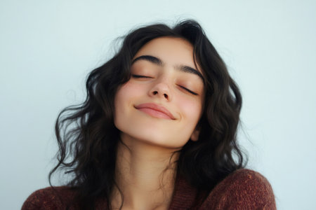 Young woman smiling gently with closed eyes, embracing a feeling of calm and relaxation. Natural beauty, serenityの素材
