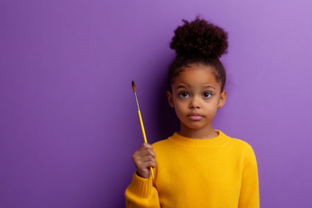 Young african american girl holding a paintbrush, looking up on a purple background, thinking about creative ideasの素材