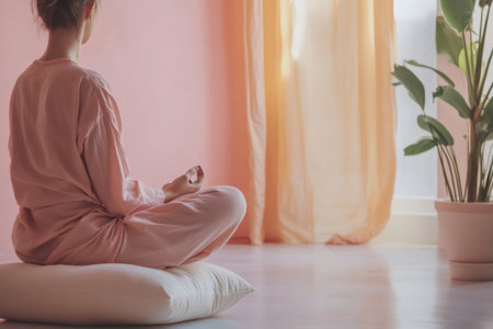 Woman sitting on cushion in lotus position, practicing mindful breathing and meditation in a peaceful home environmentの素材