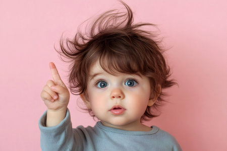Adorable baby boy with expressive blue eyes and wild hair pointing finger up, indicating attention or having a thoughtの素材
