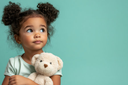 Young mixed race girl holding a teddy bear looking up, expressing thought, contemplation, and wonderの素材