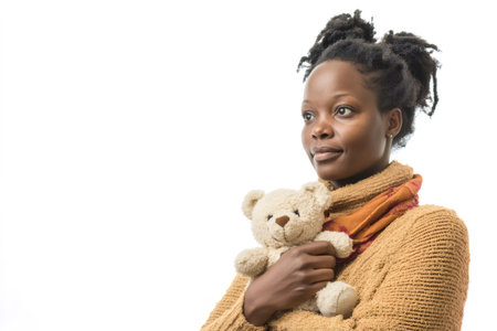 African woman holding gently a teddy bear, contemplating with a calm expression against a white backgroundの素材