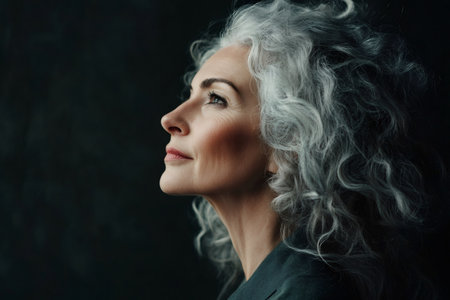 Senior woman looking up with natural curly gray hair, showing serene expression, contemplating future, embracing agingの素材