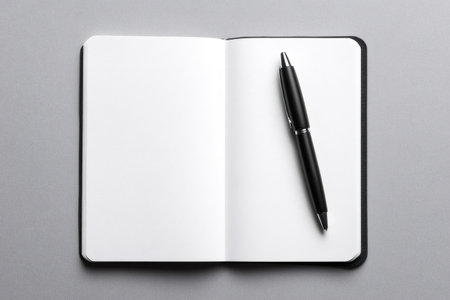Open black notebook with clean white pages and a pen, lying on a neutral gray surface. Ready for new ideas and writingの素材