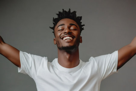 Young man standing with closed eyes and a wide smile, having his arms up in a gesture of celebration, joy, or triumphの素材