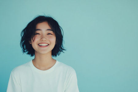 Young woman with short dark hair expressing joy, looking directly forward against a vibrant blue backgroundの素材
