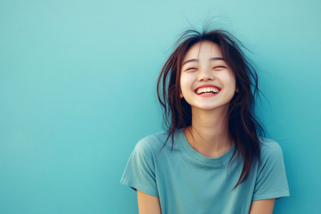 Happy young Asian woman closing her eyes and openly laughing, expressing positive emotions and carefree livingの素材