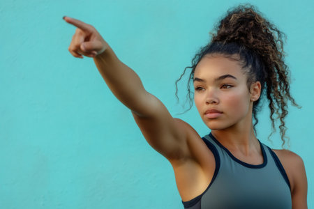 Determined young woman in workout gear pointing forward and up, symbolizing future goals, success, and aspirationの素材